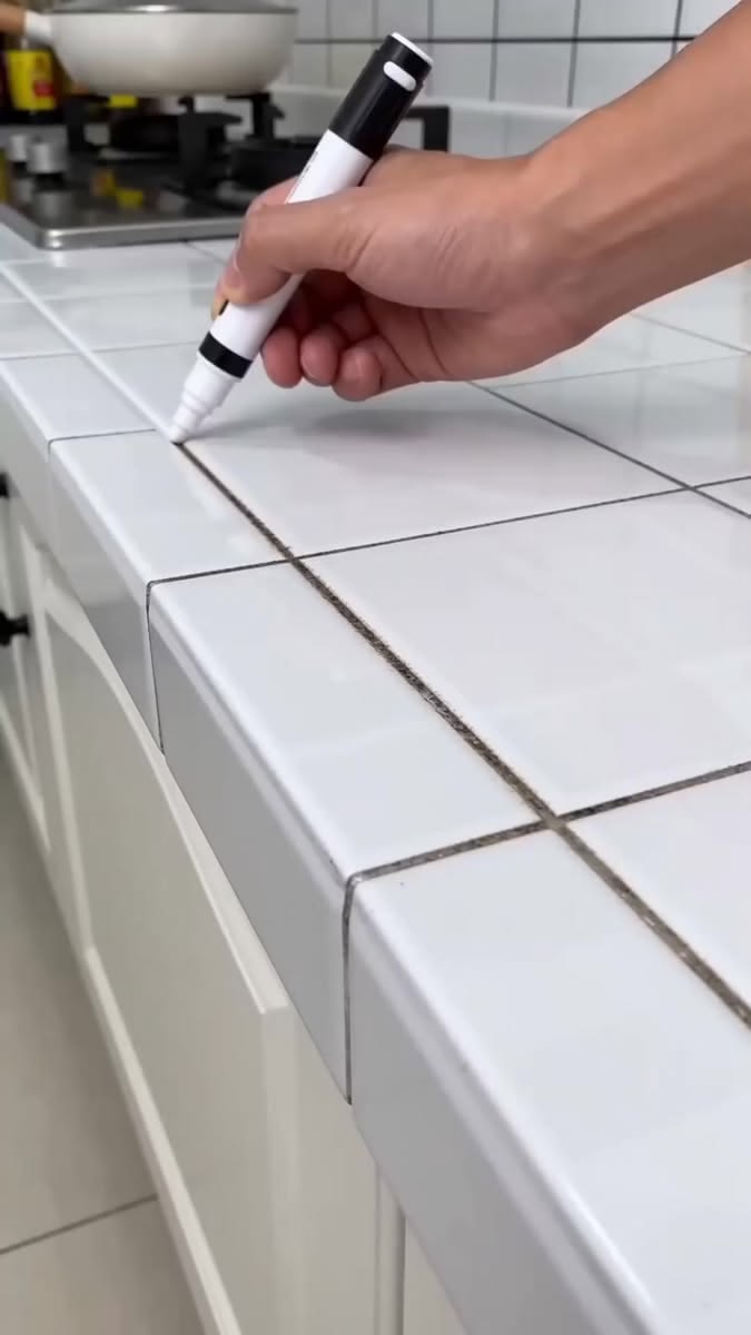 Hand using a white marker on a tiled kitchen countertop